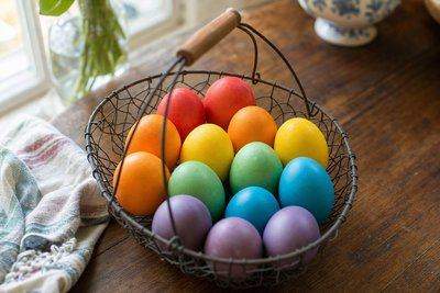 A dozen hard-boiled eggs dyed in a full rainbow of colors, arranged in a wire basket — AI-generated image